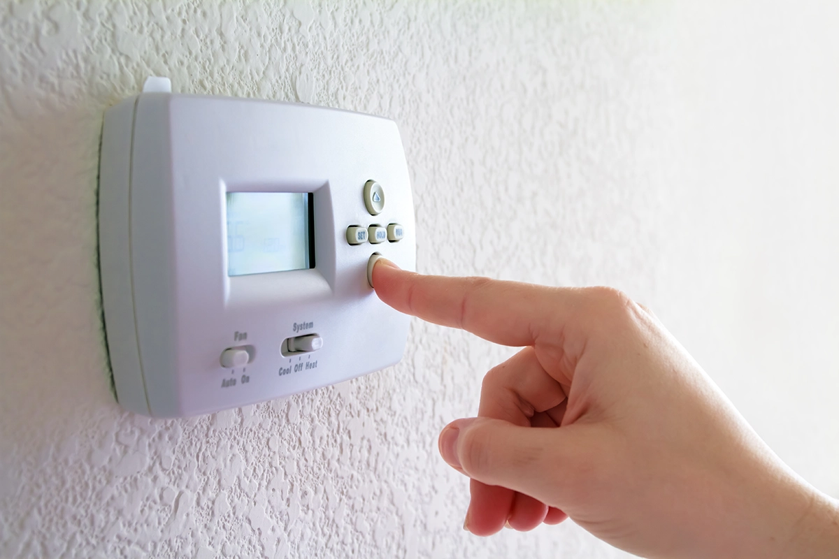 Person pressing a thermostat button while adjusting the Hold setting and checking temperature controls