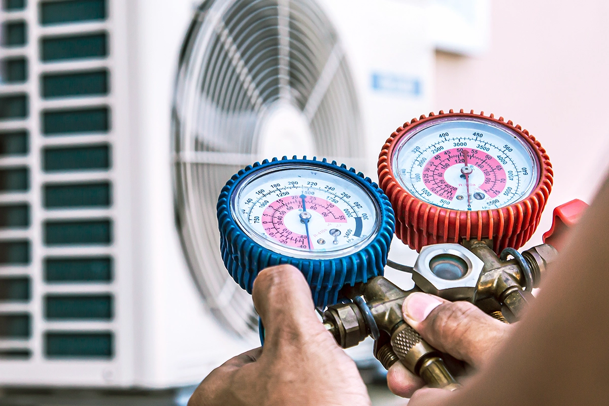 Technician checking R410A refrigerant pressure on an outdoor air conditioning unit